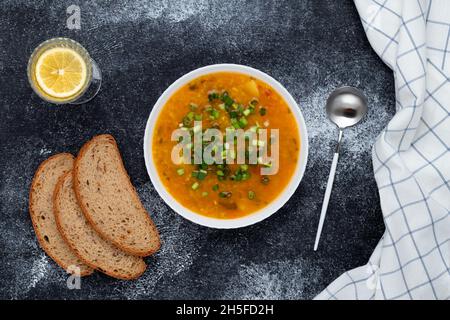 Una ciotola di zuppa di lenticchie rosse con pane sul tavolo nero. Vista dall'alto. Sfondo di cibo scuro. Un piatto di cucina greca tradizionale Foto Stock