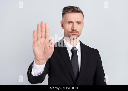 Foto di sicuro avvocato serio maturo vestito vestito nero tuta mostrando stop gesto sollevamento braccio isolato grigio sfondo di colore Foto Stock