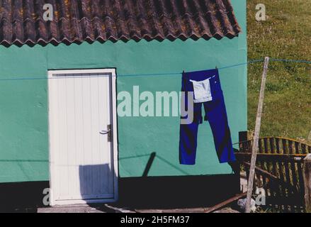 Pantaloni da lavoro blu su una linea di lavaggio di fronte ad un edificio verde Foto Stock