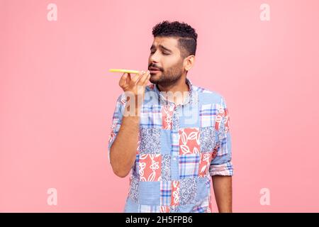 Tecnologia vocale intelligente. Bell'uomo positivo con barba in camicia blu che parla con il telefono cellulare utilizzando l'assistente virtuale, applicazione altoparlante digitale. Studio interno girato isolato su sfondo rosa. Foto Stock