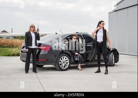 Il team armato professionale di guardie del corpo femminili e maschili protegge la persona della celebrità in limousine auto. Bodyguard e protezione personale VIP. Professate Foto Stock