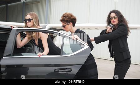 Il team armato professionale di guardie del corpo femminili e maschili protegge la persona della celebrità in limousine auto. Bodyguard e protezione personale VIP. Professate Foto Stock