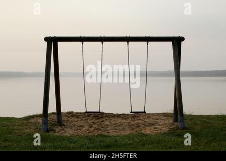 Eine leere Schaukel mit Blick auf einen leeren, dunstigen SEE. Foto Stock