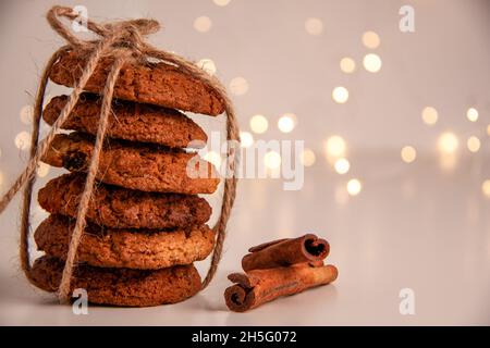 Primo piano di biscotti di farina d'avena in una pila legata con filo marrone e bastoncini di cannella su sfondo luminoso con bokeh. Concetto di cibo dolce con spazio copia Foto Stock