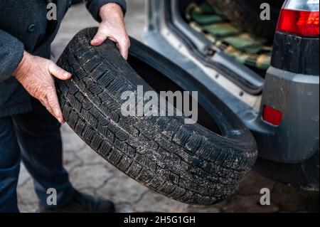l'uomo scarica una serie di pneumatici di cambio dal bagagliaio, concetto di cambio pneumatici stagionale, closeup Foto Stock