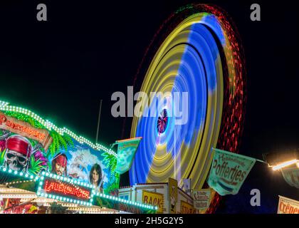 Molln, Germania, 06 novembre 2021: Lunga esposizione in una fiera annuale di divertimento viaggiante con giri veloci e bancarelle illuminate, colorato divertimento astratto b Foto Stock