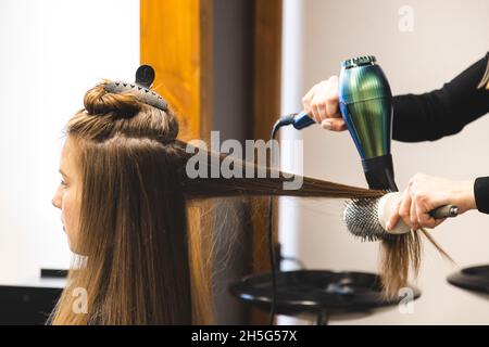 Master donna parrucchiere asciuga i capelli della ragazza con un asciugacapelli e pettini dopo il lavaggio nel salone di bellezza Foto Stock