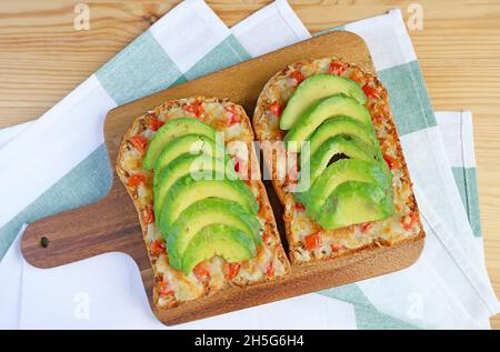 Un paio di toast fatti in casa con formaggio alla griglia, conditi con pomodoro e avocado a fette su un panino di legno Foto Stock