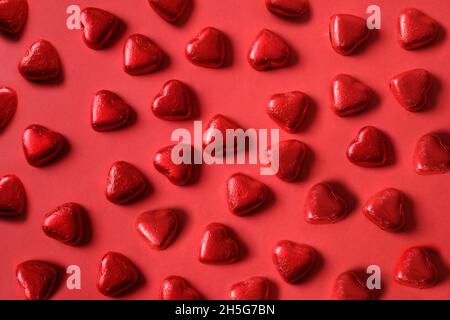 Motivo di romantici dolci al cioccolato come cuore in lamina rossa su sfondo rosso. Biglietto di auguri per San Valentino. Concetto di amore. Foto Stock