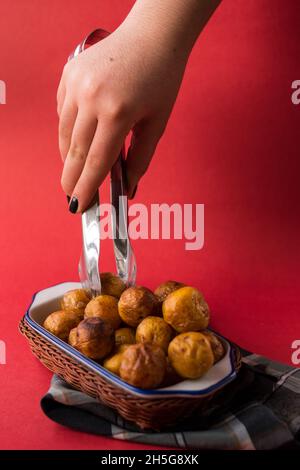 Prendere a mano un potatoe colombiano fritto da un cestino su un pezzo di tela a plaid su una superficie rossa Foto Stock
