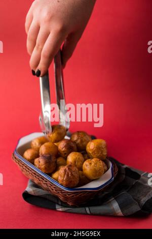 Prendere a mano un potatoe colombiano fritto da un cestino su un pezzo di tela a plaid su una superficie rossa Foto Stock