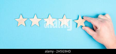 Cinque stelle su uno sfondo blu, mano mettere l'ultima stella in fila, la valutazione, dando feedback Foto Stock