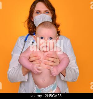 Donna pediatra che tiene un bambino in un pannolino nelle sue mani, sfondo giallo studio Foto Stock