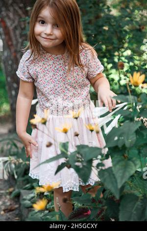 bambina piccola con fiori, fiori gialli girasole, raccoglie fiori in giardino, carino bambino di 5 anni Foto Stock