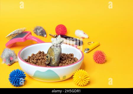 Cat alimenti secchi, accessori per la cura del corpo e giocattoli su sfondo giallo con spazio per il design. Foto Stock