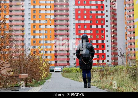 Donna solitaria in pelle nera cappotto in piedi sullo sfondo edificio di appartamenti e guardando il nuovo quartiere residenziale nella città d'autunno. Immobiliare Foto Stock