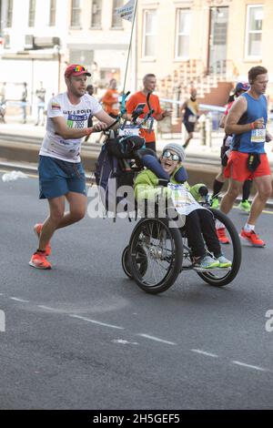 50° anniversario New York City Marathon gara nel 2021 dopo nessuna gara nel 2020 fare al Covid-19 Pandemic. L'uomo con una bandiera ecuadoriana sulla sua t-shirt corre spingendo una donna paraplicica felice aspetto di fronte a lui sulla 4th Avenue attraverso la sezione Brooklyn della corsa. Foto Stock