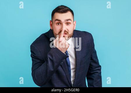 Ti stai mentire. Ritratto di arrabbiato bel borsato giovane uomo che indossa vestito di stile ufficiale in piedi, toccando il naso e mostrando il gesto della menzogna. Studio interno girato isolato su sfondo blu. Foto Stock