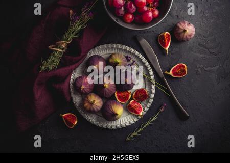 Fichi freschi biologici con uve rosse e lavanda su sfondo scuro Foto Stock