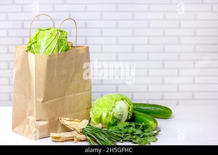 Craft sacchetto di carta con verdure verdi da online shopping a casa consegna in cucina su sfondo chiaro con spazio copia. Foto Stock