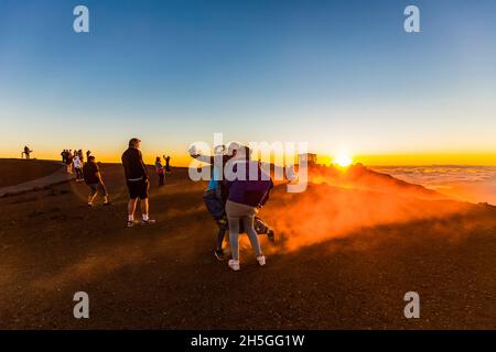 I turisti scattano fotografie e ammirano gli edifici dell'Osservatorio di Haleakala sopra le nuvole durante un tramonto colorato e suggestivo; Maui, Hawaii, United Stat Foto Stock