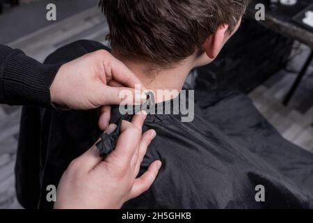 Le mani di un barbiere o di un parrucchiere preparano un cliente con capelli lunghi scuri per un servizio di taglio e di parrucchiere. Foto Stock