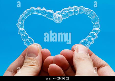 Mani che tengono gli allineatori dentali a forma di cuore su sfondo blu Foto Stock