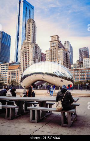 Persone sedute su panchine di fronte alla scultura di Sir Anish Kapoor Cloud Gate, soprannominata The Bean, di fronte allo skyline di Chicago, il, USA Foto Stock