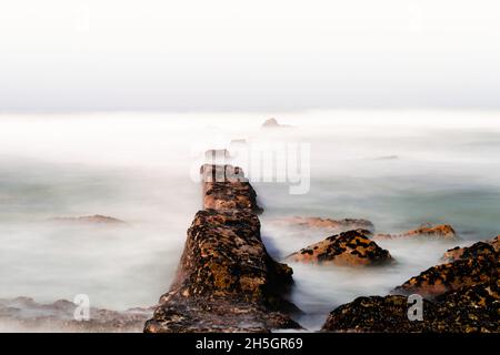 Primo piano di lunga esposizione di mare e grandi massi che si attacca dall'acqua Foto Stock