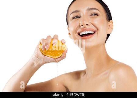 Bellezza, giovane donna con pelle raggiante, stringendo un arancio in mano, bella modella sorridente ragazza con trucco naturale, pelle raggiante e agrumi frui Foto Stock