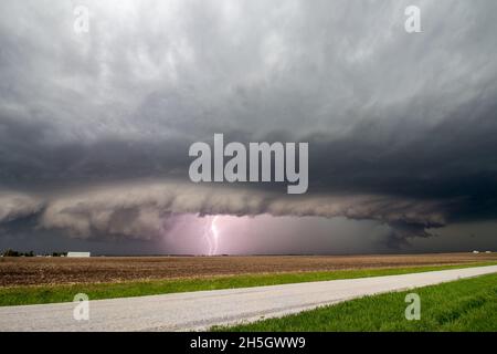 Il fulmine colpisce come un temporale supercellulare si avvicina a una strada rurale. Una nube di scaffale segna il bordo della tempesta. Foto Stock