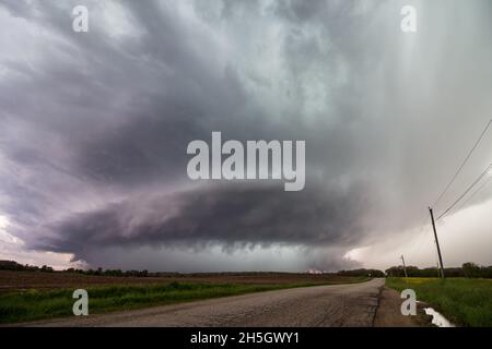 Guardando giù una strada ad una tempesta di supercelle mentre si avvicina sopra un campo di fattoria. Foto Stock