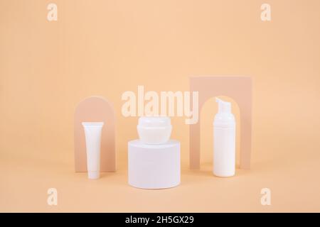 Set di bignè bianco crema su podio bianco con arco su sfondo beige. Crema di bellezza naturale cosmetici prodotto per il trucco. Presentazione del packaging o del branding Foto Stock