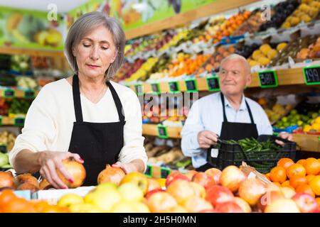 Donna lavoratore supermercato impilare frutta su scaffale in sala di vendita Foto Stock