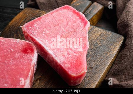 Bistecche di tonno surgelate, su tagliere di legno, su vecchio sfondo di tavola di legno scuro Foto Stock