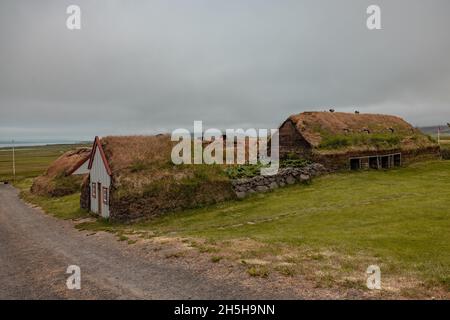 Case di erba sintetica tradizionali in Islanda ricoperte di muschio e erba, accanto ad una chiesa tradizionale in una giornata nuvolosa. Foto Stock