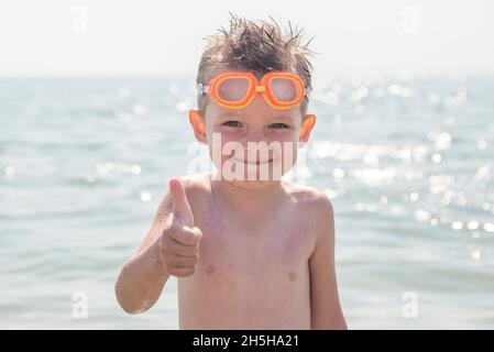 Un ragazzo in occhiali per il nuoto mostra un pollice in su sullo sfondo  del mare. Bambini in occhiali per il nuoto in mare Foto stock - Alamy