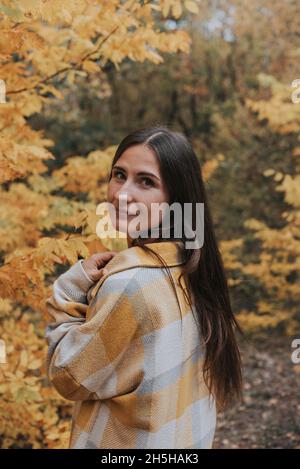 Ragazza brunetta con capelli lunghi in una camicia a quadri in un parco autunnale . Foto Stock