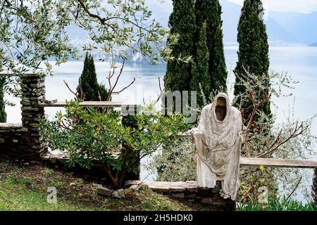 Statua fantasma su un recinto in pietra tra alberi verdi sulle rive del Lago di Como. Italia Foto Stock