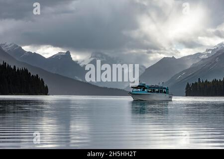 Barca sul lago Maligne, dietro la catena montuosa Queen Elizabeth Ranges con Samson Peak, cielo nuvoloso, Jasper National Park, Montagne Rocciose, Alberta Foto Stock