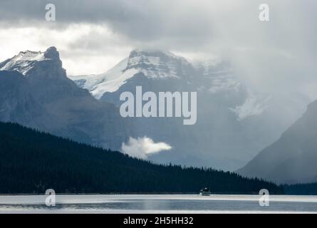 Barca sul lago Maligne, dietro la catena montuosa Queen Elizabeth Ranges con Samson Peak, cielo nuvoloso, Jasper National Park, Montagne Rocciose, Alberta Foto Stock