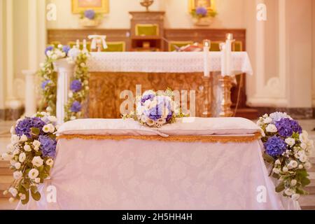 Colorato bouquet nuziale composto da fiori bianchi e blu che giacciono su cuscini sopra la panca di nozze di fronte all'altare della chiesa Foto Stock