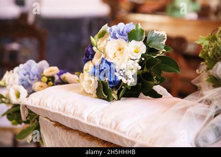 Colorato bouquet nuziale composto da fiori bianchi e blu che giacciono su cuscini sopra la panca di nozze di fronte all'altare della chiesa Foto Stock