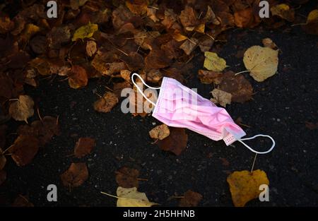 La maschera di protezione rosa scartata si trova a terra nelle foglie autunnali, Corona Crisis, Stoccarda, Baden-Wuerttemberg, Germania Foto Stock