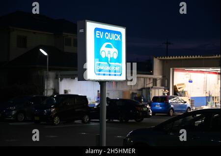 Punto di ricarica rapida EV per veicoli elettrici. Segnale di accensione della luce blu. Negozio di riparazione in background. Foto Stock