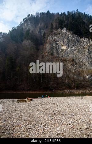 I bambini giocano ai piedi di un'alta parete rocciosa coperta da fitta foresta mista sul fiume Dunajec in autunno | Dunajec River Gorge in autunno, Pieniny Foto Stock