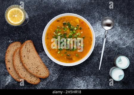Ciotola di zuppa di lenticchie vegetariana con lenticchie rosse e pane marrone sul tavolo scuro. Vista dall'alto. Sfondo alimentare. Un piatto tradizionale di cucina greca Foto Stock