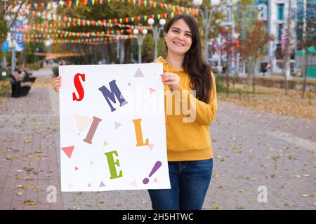 Una donna tiene un poster con il testo Smile nel parco. Foto Stock