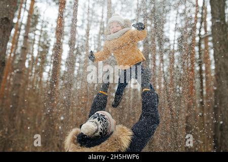 Papà che solleva il suo piccolo figlio felice in aria durante una passeggiata in famiglia nella foresta Foto Stock