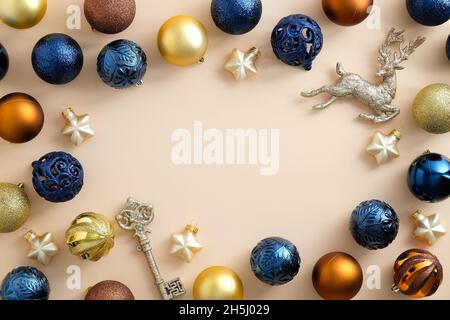 Moderna composizione natalizia. Cornice in blu, bronzo e oro baubles, stelle, chiave, cervo su sfondo beige pastello. Natale biglietto d'auguri templa Foto Stock